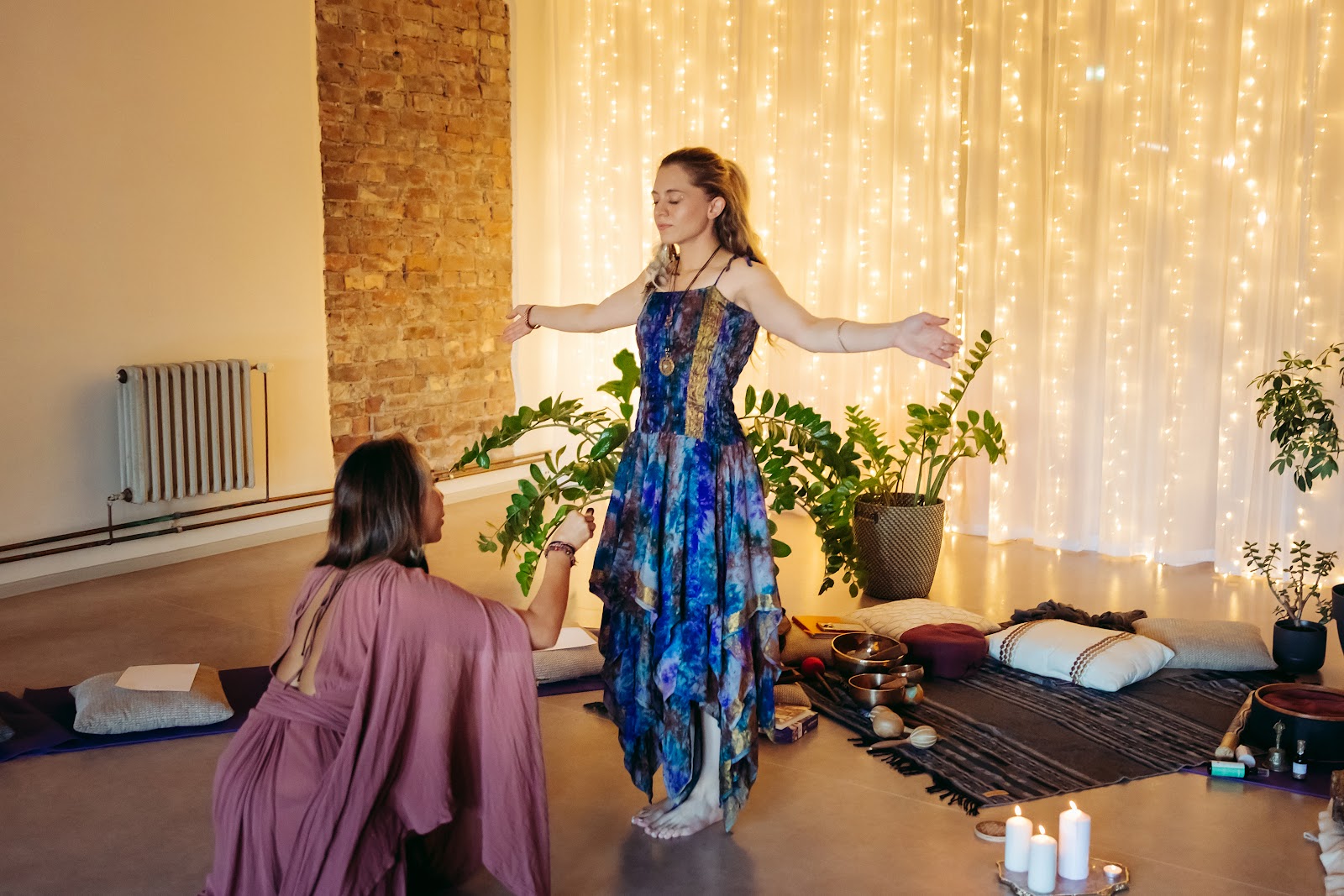 Sabrina Stocker in ceremony, arms open, being smoke-cleansed before the fairy-light curtain in Tallinn.